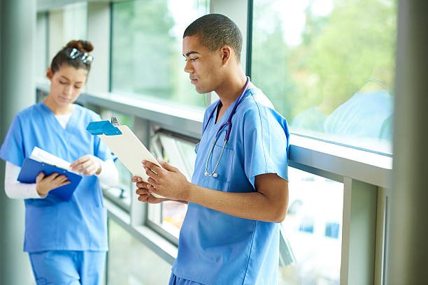 a young male and female nurse stand in the corridor of the hospital checking their medical notes .